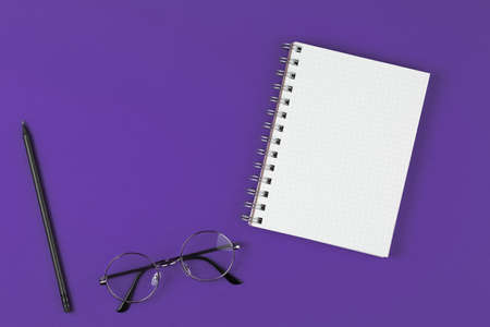 open notebook with pencil and glasses on the violet background, school notebook on the purple desk, office desk with notebookの写真素材