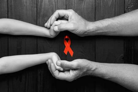 AID red ribbon in hand on a black wooden background, a symbol of the fight against HIV, AIDS and cancer. concept of helping those in need.black and white.の写真素材