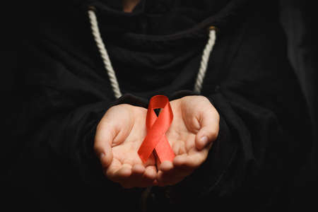 child with AID red ribbon on a dark background. the boy holds the symbol of the fight against HIV,...