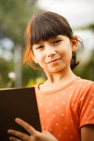 Cute girl in T-shirt is reading outdoors on an sunny day. Preparation for school and international...