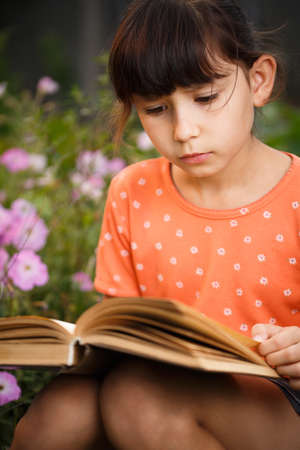 Cute girl in T-shirt is reading outdoors on an sunny day. Preparation for school and international...