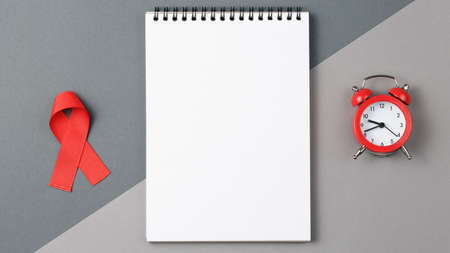 Red ribbon on notebook on gray background, symbol of the fight against HIV and AIDS. helping cancer...