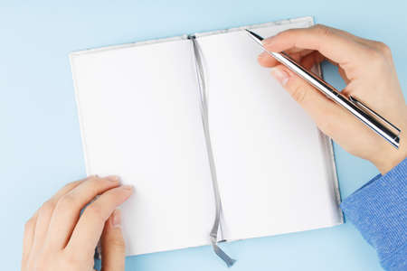 notepad in her hands on a blue background top view, the girl writes into the notebook the to-do list...