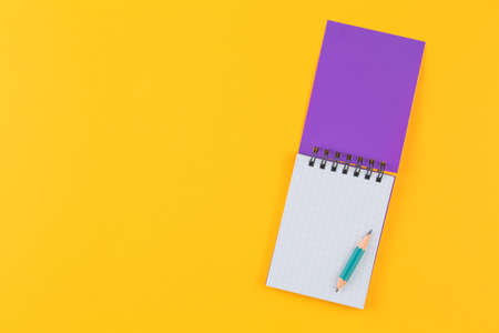 little purple notepad with pencil on isolated yellow background flat lay. top view. school concept,...