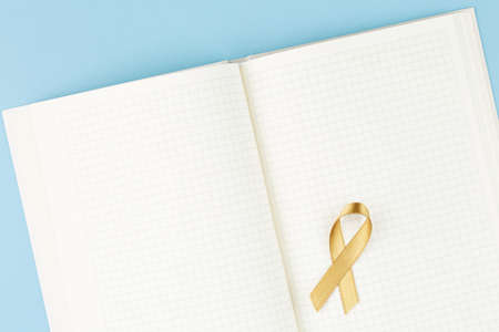 gold ribbon on open notebook isolated on blue background, childhood cancer and symbol of helping...