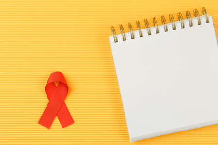 red aids ribbon on open notebook isolated on yellow background, aids day and symbol of helping...