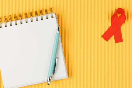 red aids ribbon on open notebook isolated on yellow background, aids day and symbol of helping cancer patients vertical viewの写真素材