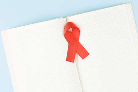 red aids ribbon on open notebook isolated on blue background, aids day and symbol of helping cancer patientsの写真素材