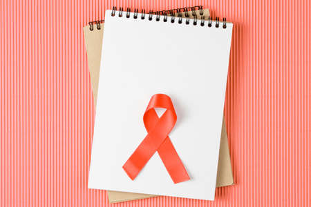 red aids ribbon on open notebook isolated on Living Coral background, aids day and symbol of helping cancer patients vertical viewの写真素材
