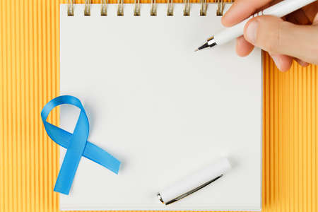 blue prostate ribbon on open notebook isolated on yellow background, prostate cancer and symbol of...