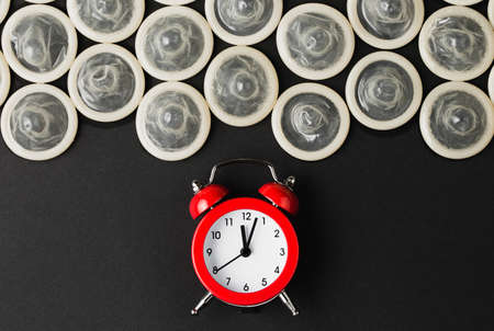 red alarm clock with condoms on black background, flat lay, concept of fight against HIV and aidsの写真素材