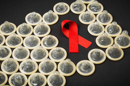 Red AIDS ribbon with condom on black background, symbol of the fight against AIDS and HIV. Flat lay.の写真素材