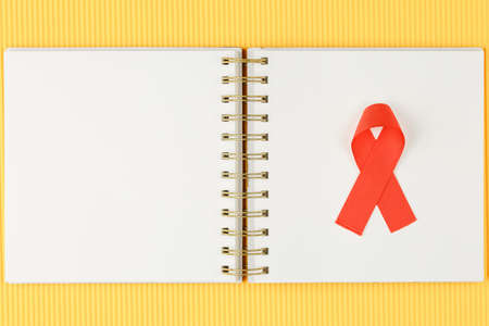 red aids ribbon on open notebook isolated on yellow background, aids day and symbol of helping cancer patients vertical viewの写真素材