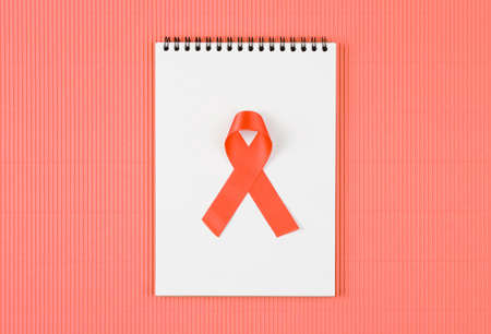 red aids ribbon on open notebook isolated on Living Coral background, aids day and symbol of helping...