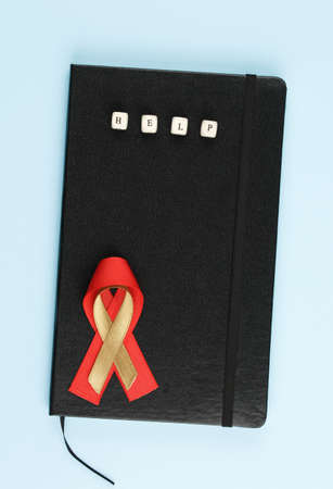 red aids ribbon on black leather notepad isolated on blue background, aids day and symbol of helping...