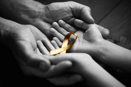 golden ribbon childhood symbol of the fight against cancer in children in hands on a dark background. concept of helping patients with sarcoma and bladder cancer.black and white.の写真素材