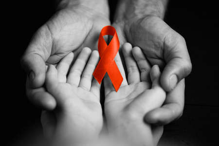 child with AID red ribbon on a dark background. the boy holds the symbol of the fight against HIV,...
