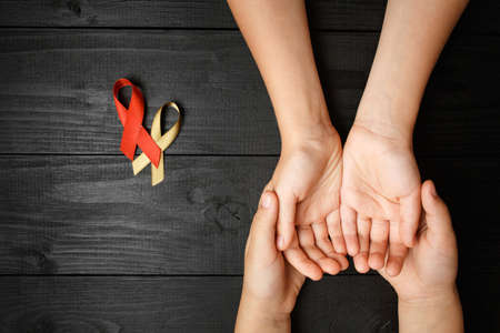 golden adn AID ribbon childhood symbol of the fight against cancer in children in hands on a dark...