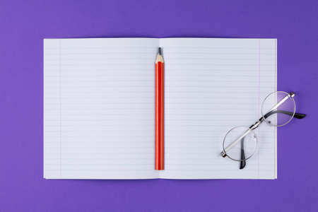 open notebook with red pencil and glasses on the violet background, school notebook on the purple desk, office desk with notebookの写真素材
