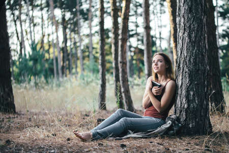 girl under a tree dreams with a book in her hands. young woman reads a book while traveling in the forestの写真素材