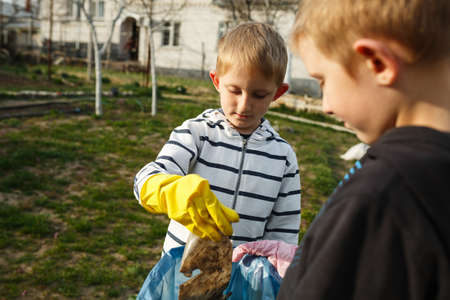 Two little boys in the park collect plastic bottles in a plastic bag, children scavenge on the streets.Environmental consciousness and awareness.の写真素材