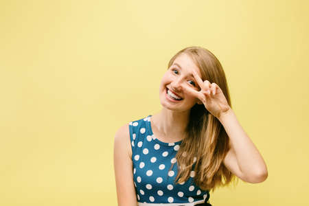 beautiful teen girl in pea dress on yellow background shows thumbs up, model in studio on yellow backgroundの写真素材