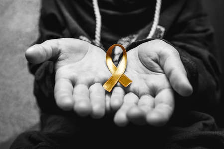 golden ribbon childhood symbol of the fight against cancer in children in hands on a dark background. concept of helping patients with sarcoma and bladder cancer.black and white.の写真素材