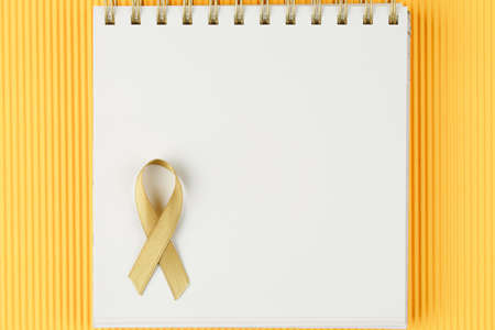 gold ribbon on open notebook isolated on yellow background, childhood cancer and symbol of helping AIDS patientsの写真素材