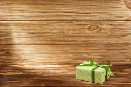 Gift box with green ribbon on wooden background top view. New year and Christmas holiday concept. Flat lay with copy space. Discount gift for sale day.の写真素材