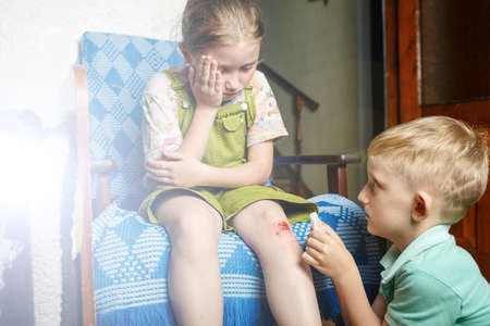A little girl hurt her knee, a boy heals her wound. a scratched knee. brave girl