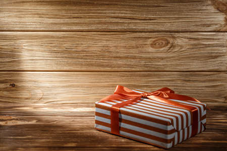 Gift box with orange ribbon on wooden background top view. New year and Christmas holiday concept. Flat lay with copy space. Discount gift for sale day.の写真素材