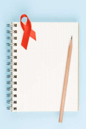 red aids ribbon on open notebook isolated on blue background, aids day and symbol of helping cancer patients vertical viewの写真素材