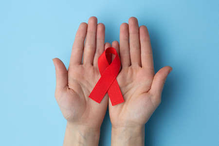 aids red ribbon on the palm and on a blue background, hiv ribbon on kraft paperの写真素材