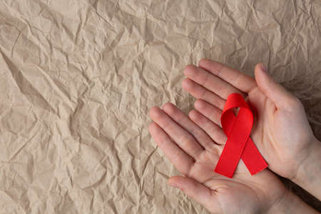 aids red ribbon on a palm and on a craft background, hiv ribbon on kraft paperの写真素材