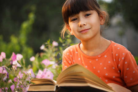 Cute girl in T-shirt is reading outdoors on an sunny day. Preparation for school and international literacy day. Back to school concept.の写真素材