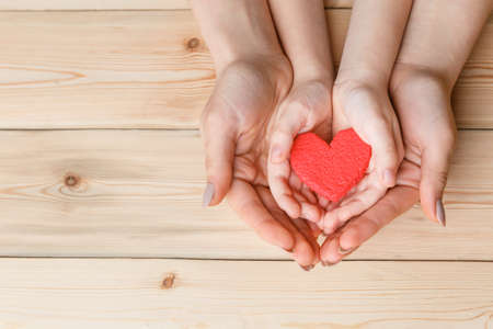 hands with red heart, top view on white and wooden background