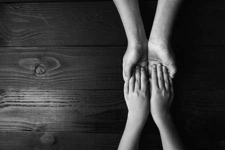top view arms stretches out and holds one another on black wooden background. joint support and assistance in the community, children's hands help each other with support.black and white.の写真素材