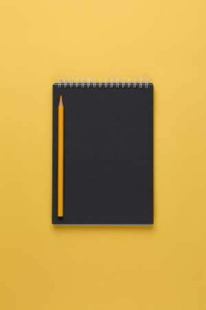 notebook with black paper and with a pencil on a yellow background top view, blank sheet for writing purposes, business concept flat layの写真素材