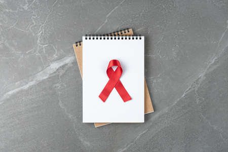 red aid ribbon on notebook on gray marble table, top view. symbol of fight against cancer, hiv and aids, flat lay.の写真素材
