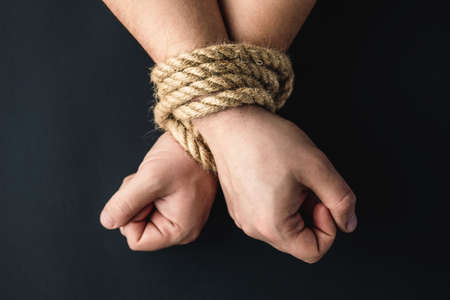 hands tied with a rope on a black background, the concept of stealing people, right day