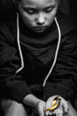 golden ribbon childhood symbol of the fight against cancer in children in hands on a dark background. concept of helping patients with sarcoma and bladder cancer.black and white.の写真素材