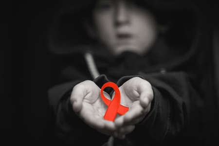 child with AID red ribbon on a dark background. the boy holds the symbol of the fight against HIV, AIDS and cancer. concept of helping those in need.black and white.の写真素材
