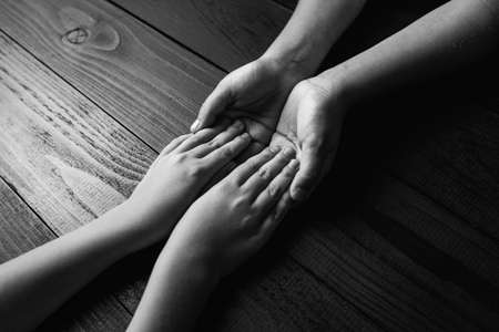 top view arms stretches out and holds one another on black wooden background. joint support and assistance in the community, children's hands help each other with support.black and white.の写真素材