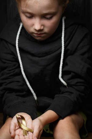 golden ribbon childhood symbol of the fight against cancer in children in hands on a dark background. concept of helping patients with sarcoma and bladder cancerの写真素材