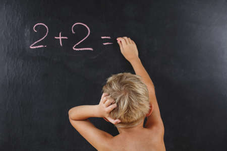 little boy without a T-shirt thinks on the blackboard, the child writes on the school chalkboard a chalk, a summer schoolの写真素材