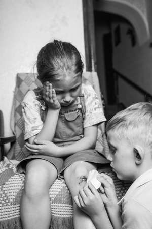 A little girl hurt her knee, a boy heals her wound. a scratched knee. brave girl.black and white.の写真素材