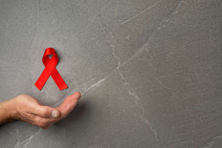 AID red ribbon in hand on gray background, symbol of the fight against HIV, AIDS and cancer. concept...