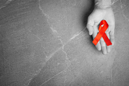 red ribbon in hands on gray background, World Cancer Day, symbol of fight against HIV, AIDS and cancer. concept of helping those in need. black and white.の写真素材