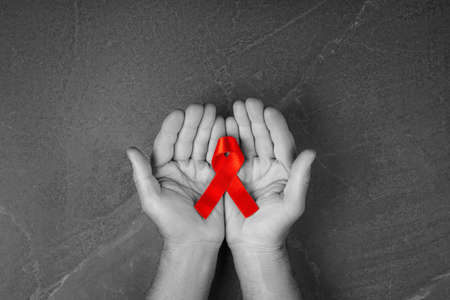 red ribbon in hands on gray background, World Cancer Day, symbol of fight against HIV, AIDS and cancer. concept of helping those in need. black and white.の写真素材