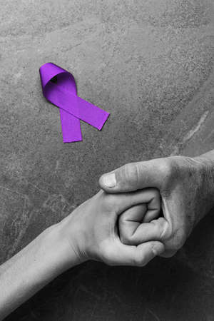 Hands holding purple ribbons top view on gray wooden background. Alzheimers disease, epilepsy, fibromyalgia awareness, world cancer day. black and white. symbol of fighting child abuse.の写真素材